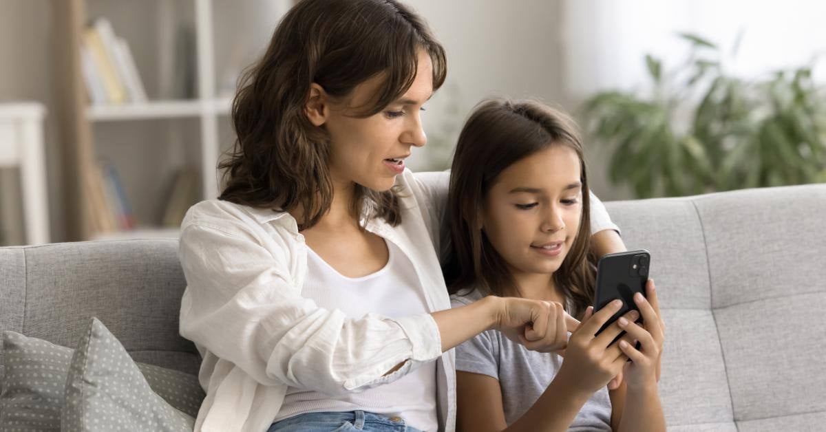 Mother and daughter sitting on couch scrolling on phone