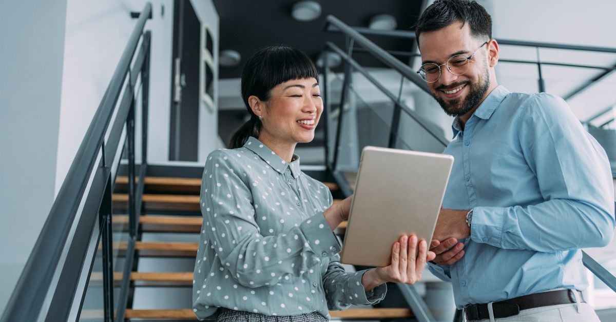 man and woman smiling while discussing content on a tablet